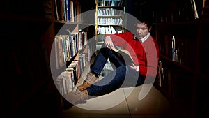 Student sitting on floor in library, reading book