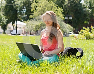 Student sitting on grass with laptop. Beautiful young woman with notebook online in the park. Outdoor. Sunny day. Back to school.