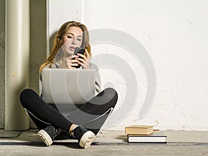 Student sitting with her laptop and looking at her smartphone