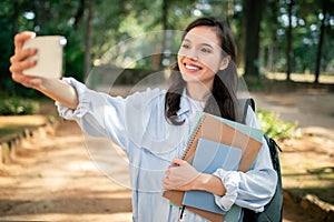 Student smiling taking selfie with phone at public park