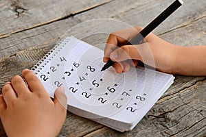 Student solves multiplication examples. Child holds a black marker in his hand and writes answers