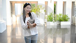 Student standing in front of the campus building and holding her textbook