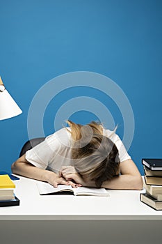 Student studying exam and sleeping on books on a blue background. Tired student girl with glasses sleeping on the books