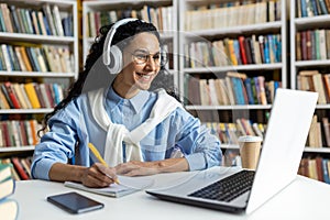 Student studying in library with laptop and headphones