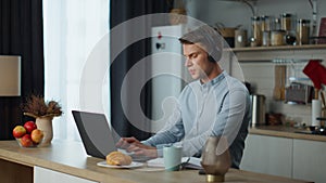 Student studying online laptop at kitchen with headphones. Man listening webinar