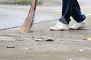 Student sweeping dried leafs on the floor in school