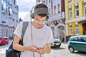 Student teenager in headphones with backpack looks into the smartphone screen