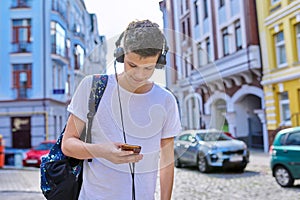 Student teenager in headphones with backpack looks into the smartphone screen