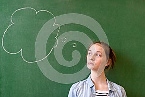 Student thinking blackboard concept. Pensive girl looking at thought bubble on chalkboard background. Caucasian student.