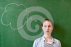 Student thinking blackboard concept. Pensive girl looking at thought bubble on chalkboard background. Caucasian student.