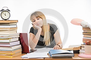 Student tired of looking at laptop at the desk in the library crammed with stacks of books