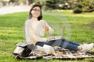 Student using laptop, sitting in the park near campus