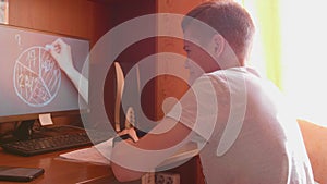 The student watches the lesson online and learns at home. A young guy does his homework while looking at the computer