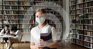 Student wear face mask standing in library looking at camera