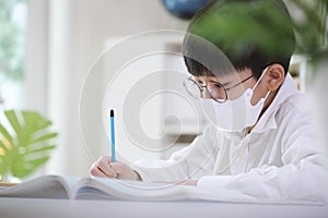 A student wearing a mask sitting at a desk and studying hard while concentrating on studying