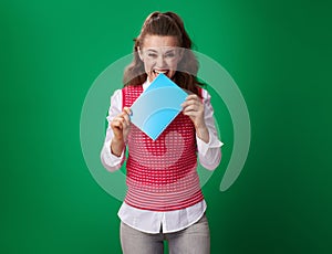 Student woman biting blue notebook isolated on green background