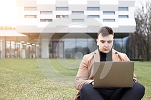 Student working on a laptop outdoor. Man sits with a laptop in his hands on the backcground of a business center