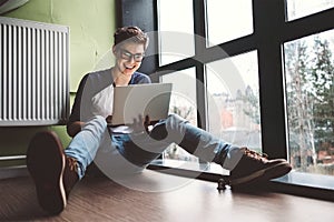 Student working with laptop sits on the floor near the window