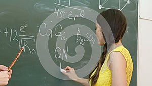 Student writing chemical symbol on blackboard.