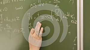 Student writing mathematical formula on blackboard