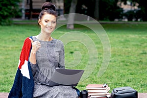 Student young woman is showing thumb up and uses laptop at the park