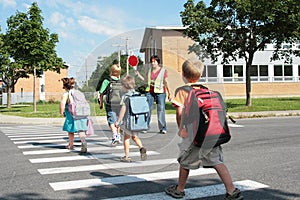 Un punto de vista de los estudiantes de primaria de cruzar la calle en su camino a la escuela bajo la atenta mirada de un guardia de cruce.