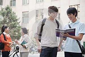 Students discussing and looking at the book, another student talking with professor on the background