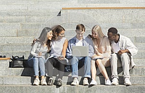 Students doing homework on laptop, sitting on stairs in city