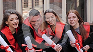 Students graduates in academic gowns with diplomas in hand posing for camera.