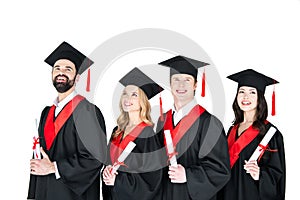 Students in graduation gowns and mortarboards holding diplomas on white