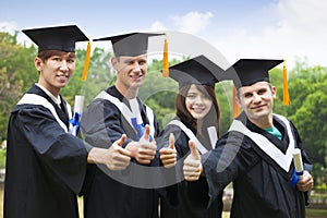 students in graduation gowns showing diplomas with thumbs