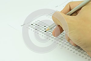 Students hand holding pencil writing selected choice on answer sheets and Mathematics question sheets. students testing doing exam