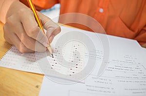 Students hands taking exams, writing examination room with holding pencil on optical form of standardized test with answers and e