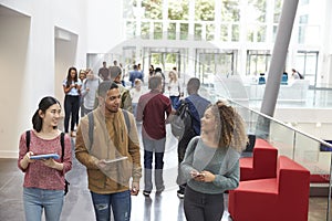 Students holding tablets and phone talk in university lobby