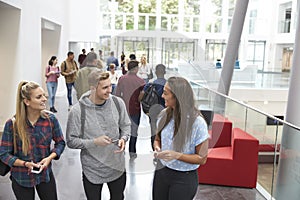 Students holding tablets and phone talk in university lobby