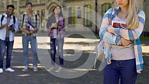 Students laughing and pointing to lonely sad girl standing aside, cruel bulling