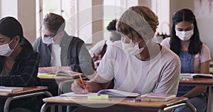 Students learning and writing in school during covid with mask during a test, studying or exam a classroom. High school