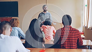 Students listening teacher's answer standing in front of students' desk. Schools and people concept