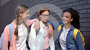 Students offending smart classmate in eyeglasses putting hands on shoulders photo