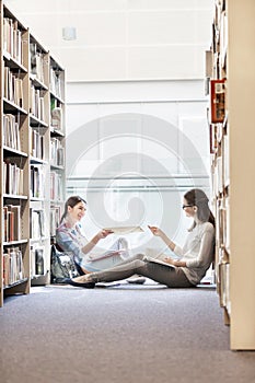 Students passing book while sitting at university library