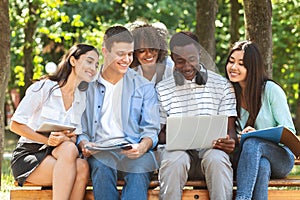 Students Passtime. College Friends Sitting Outdoors With Laptop, Watching Videos Together photo