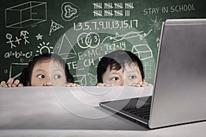 Students peeking laptop with scribble on chalkboard