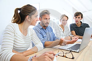 Students with professor in classroom working on laptop