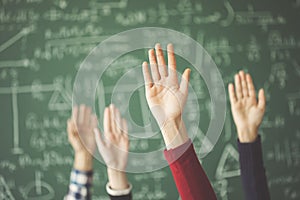 Students raised up hands green chalk board in classroom