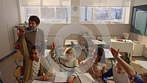 Students raising hands at lesson in classroom. Schoolteacher asking questions