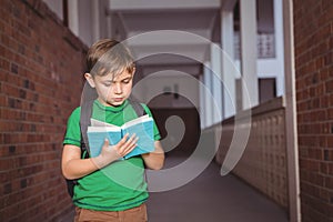Boy student reading blue hardcover book in school corridor carrying black backpack near lockers