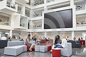 Students sit talking under AV screen in atrium at university photo