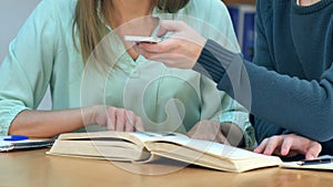 Students with smartphones taking picture of books page and making cheat sheet in school library