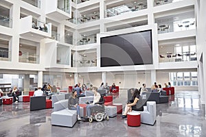 Students socialising under AV screen in atrium at university