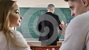 Students talk and interfere with the lesson. The teacher writes formulas on the blackboard